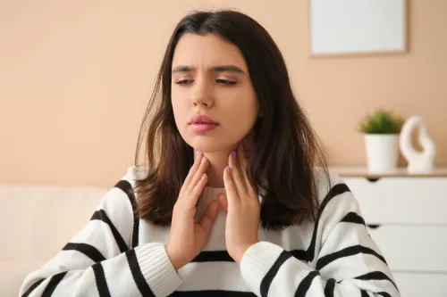 A young woman with a concerned expression gently touches her neck, symbolizing the discomfort, fatigue, and hormonal imbalance often associated with hypothyroidism.